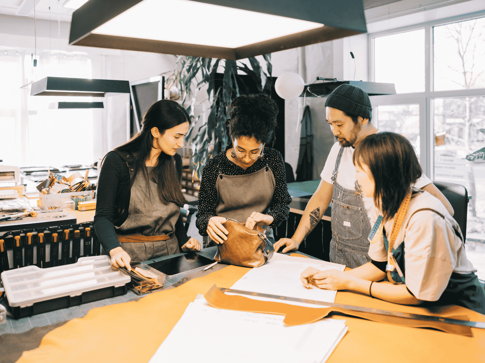 Leather craft artisans collaborating in a workshop on handmade bag design and material selection.