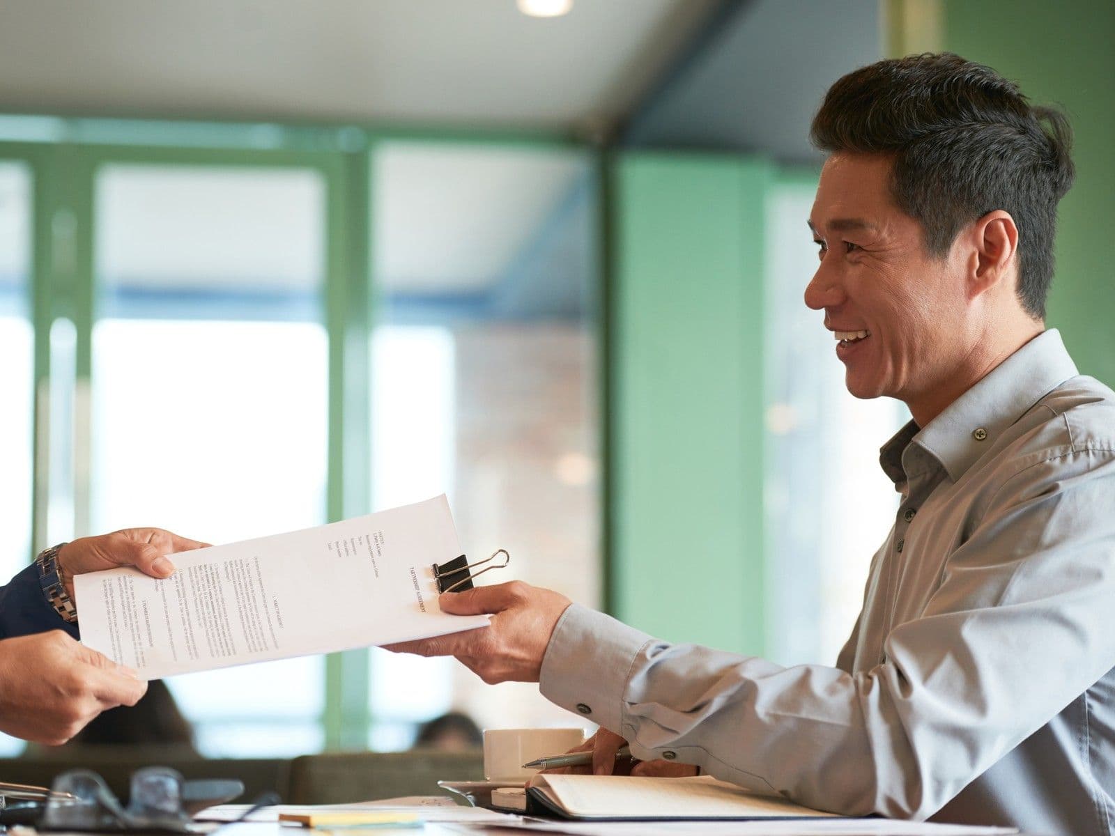 Manager handing a signed document to a colleague, showing delegated signing authority in practice